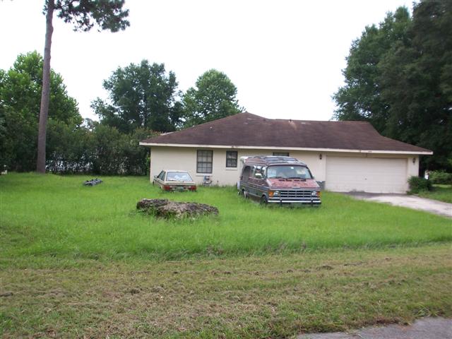 house with over grown grass and junk car in the yard